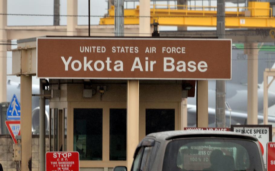 A brown sign reading “Yokota Air Base” on top of a guard post at the entrance to a military base.
