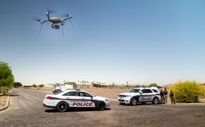 A drone hovers above two police cars.
