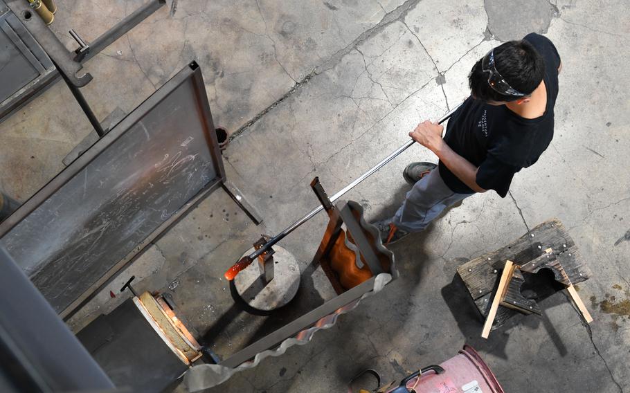 A glass blower inserts molten glass into a furnace.