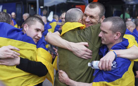 Soldiers with Ukrainian flags draped over their shoulder hug each other after a prisoner exchange.