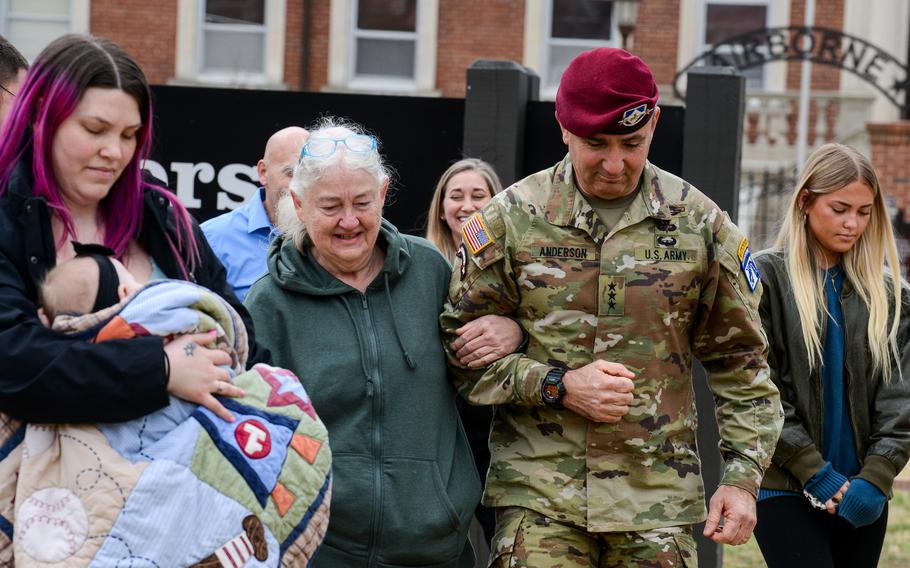 Two women walking with a soldier as others follow behind them.