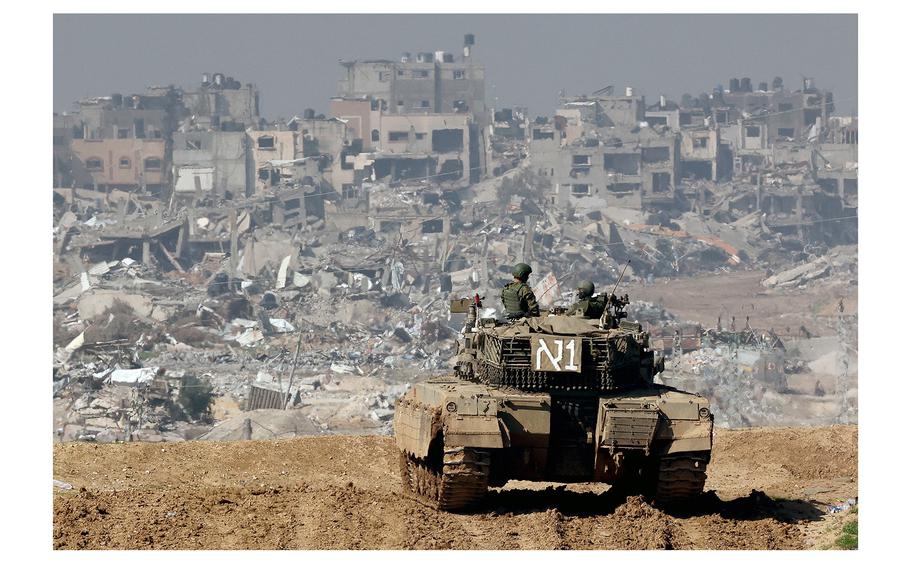 An Israeli tank rolls along the fence along the border with the Gaza Strip on Jan. 19, 2024, as damaged buildings are seen in the Gaza strip amid continuing battles between Israel and the militant group Hamas.