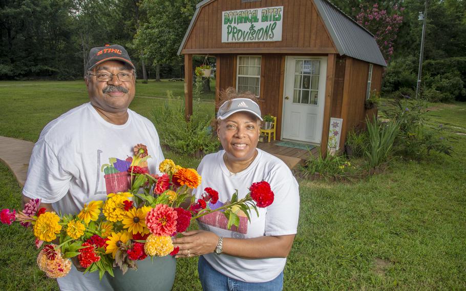 A man and woman hold bunches of flowers in front of a shed on their farm.