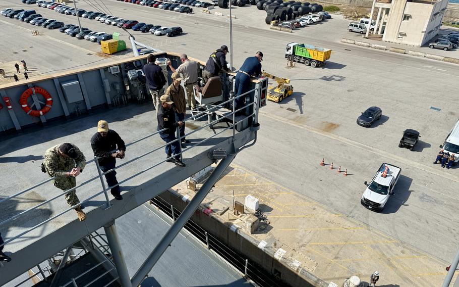 Crew members stand on the deck of a docked ship.