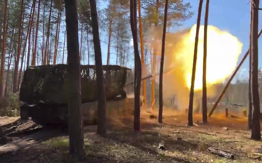 A ball of flames shoots out of the gun barrel of a tank as it fires from between thin trees.