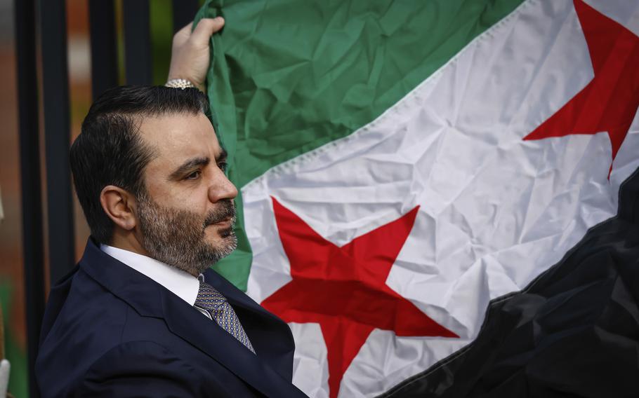 A man in a suit and tie seen from the shoulders up, holding a large flag.