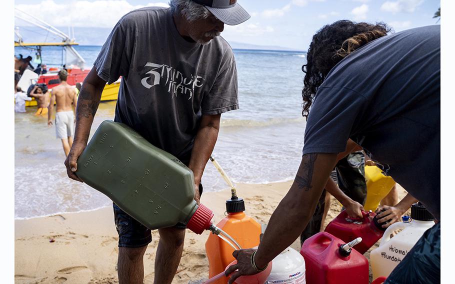 Local residents divide rations of gasoline near where a boat full of supplies was offloaded in the Kahana area of Hawaii, on Friday, Aug. 11, 2023.