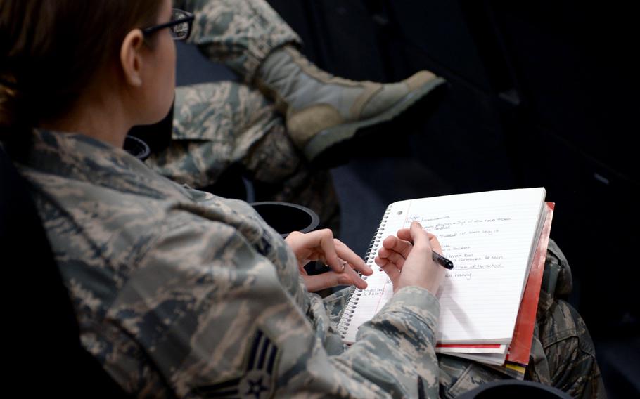 A service member with the U.S. Air Force seen from over the shoulder, holding a notepad and pen.