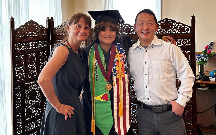 Cathy Rice poses in her cap and gown, adorned with U.S. and Guyanese flags, ahead of her graduation from Kadena High School at Kadena Air Base, Okianwa, Firday, June 2, 2023. She is with her mother, Tracy, and brother, Eric.