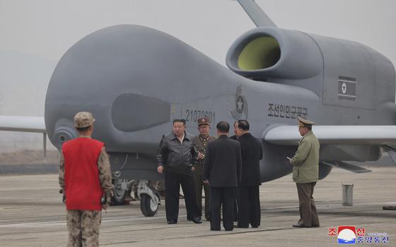 Kim Jong Un, center left in a black jacket, stands by what appeared to be a large reconnaissance drone