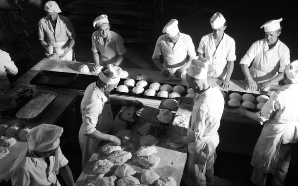 A black and white photo of bakers handling dough on tables.