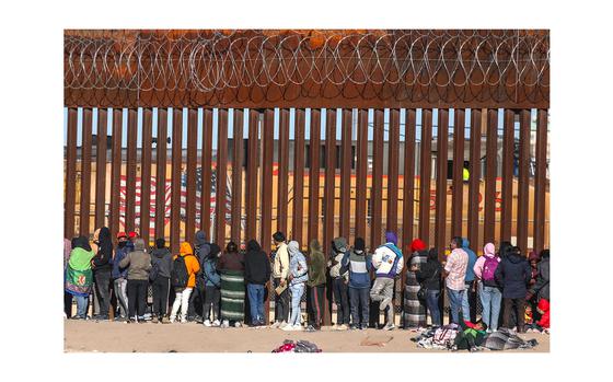 Migrants queue at the border wall to be received by Border Patrol agents after crossing the Rio Grande river from Ciudad Juarez, Chihuahua state, Mexico to El Paso, Texas, on Dec. 21, 2022.  