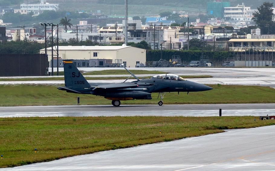 A military fighter jet on a runway with a cityscape in the background.