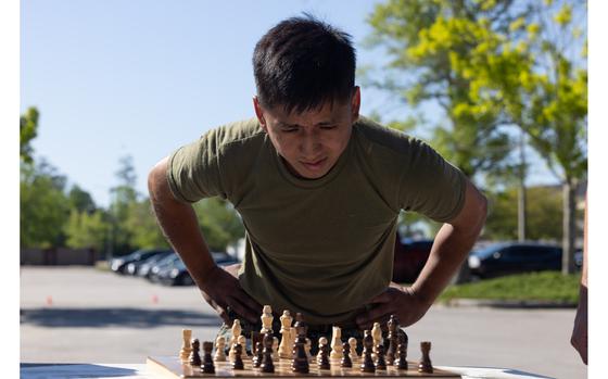 U.S. Marine Corps Cpl. Uziel Pacheco-Pacheco, a student with Distribution Management Instruction Company, Ground Supply School, and a native of Phoenix, plans a chess move on a chessboard during a physical training event on Camp Gilbert H. Johnson, North Carolina, April 16, 2025. GSS conducted training to build motivation, instill camaraderie, improve unit cohesion, and cultivate the ability to make complex decisions while under physical stress. (U.S. Marine Corps photo by Lance Cpl. James Bricker)