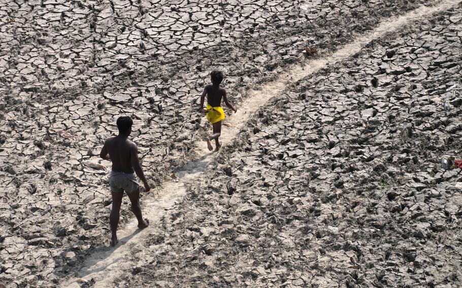 A man and a boy walk across an almost dried up bed of river Yamuna following hot weather in New Delhi, India, Monday, May 2, 2022. An unusually early and brutal heat wave is scorching parts of India, where acute power shortages are affecting millions as demand for electricity surges to record levels.