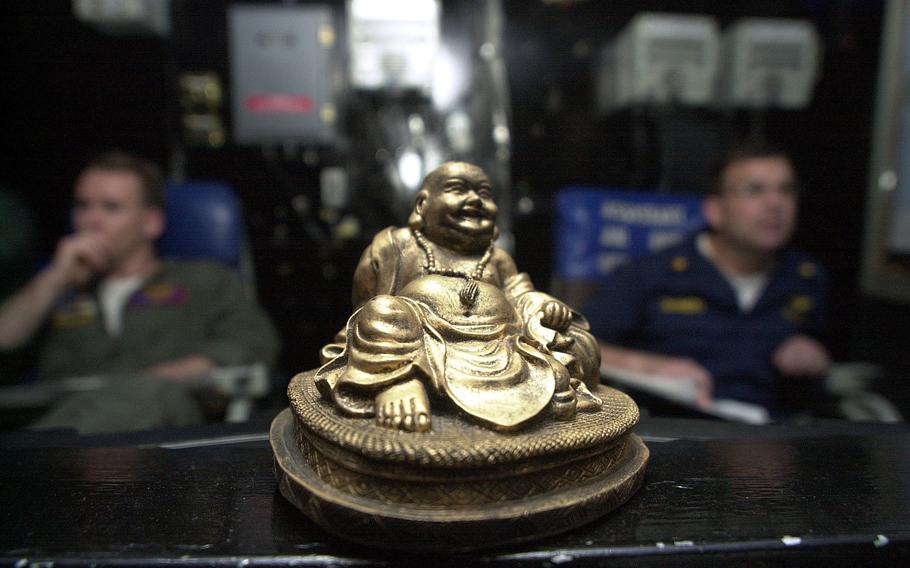 A Buddha statuette sits on a console in the air traffic control center aboard the USS Kitty Hawk, while officers monitor air traffic above the carrier on Monday, April 15, 2002.