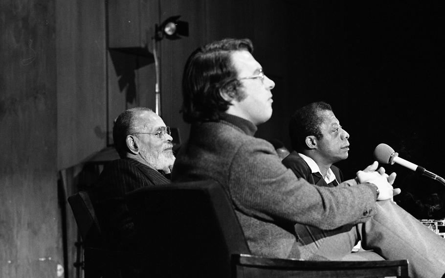 Moderator Gary Stevens and authors Chester Himes and James Baldwin listen to a question from an audience member.