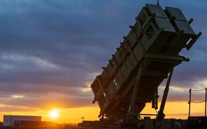 A Patriot missile defense system launcher positioned at an elevated angle against a sunset sky. 