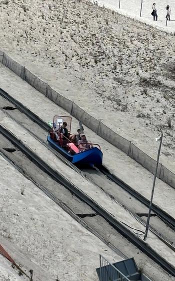A track system transports people to the top of a hill made of sand.