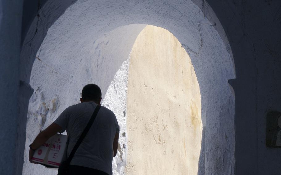 A man carries provisions up a steep alleyway in the compact, hilltop white village of Pyrgos on Santorini island, Greece, on July 1, 2021. Pyrgos sits removed from the tourist trail in the bucket-list island destination, among volcanic vineyards that grow the native grape Assyrtiko. 