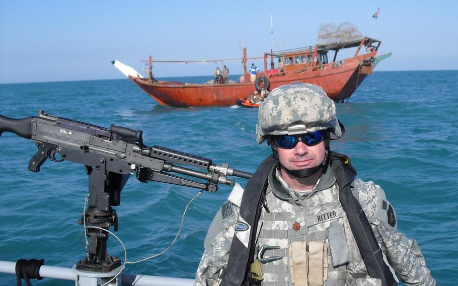 Ritter in uniform on a boat next to a weapon with a vessel in the background.