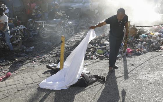 A person lifts a sheet to look at the identity of a body lying on the ground after an overnight shooting in the Petion Ville neighborhood of Port-au-Prince, Haiti, Monday, March 18, 2024. (AP Photo/Odelyn Joseph)