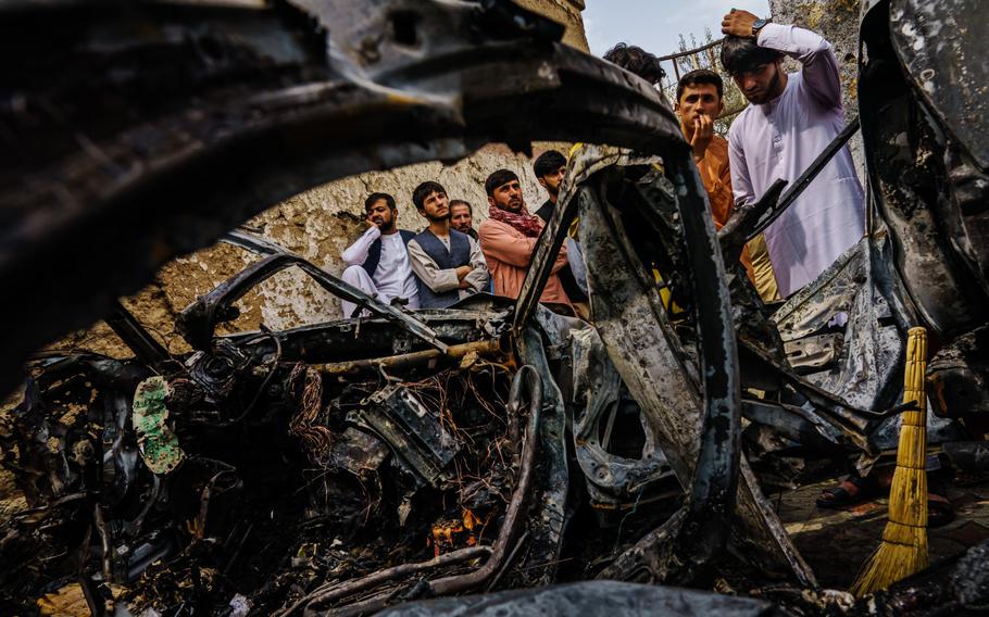 Relatives and neighbors of the Ahmadi family gather around the incinerated husk of a vehicle targeted and hit earlier Sunday afternoon by an American drone strike, in Kabul, Afghanistan, Monday, Aug. 30, 2021.