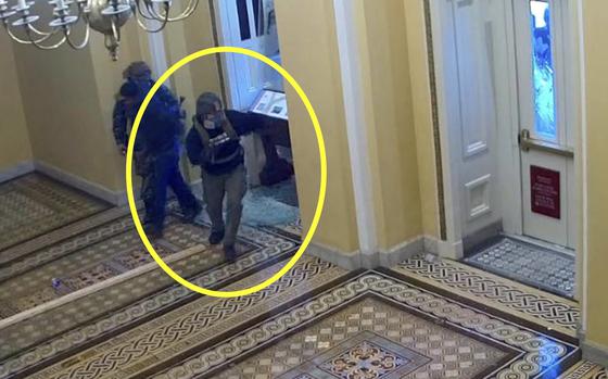 Video security footage shot from above shows two men in helmets and gas masks entering an ornately-carpeted hallway in the U.S. Capitol building.