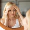 Senior woman looking at mirror and touching forehead, upset aged lady examining fine lines on her face, suffering skin aging, selective focus on reflection