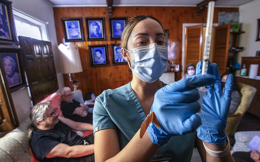 Licensed vocational nurse Angela Tapia prepares a dose of the Moderna COVID-19 booster vaccine at the Los Angeles home of Louis Salazar Jr., 64, left, and his father, Louis Salazar Sr., 90. They both received the booster, along with Maria Salazar, 88. 