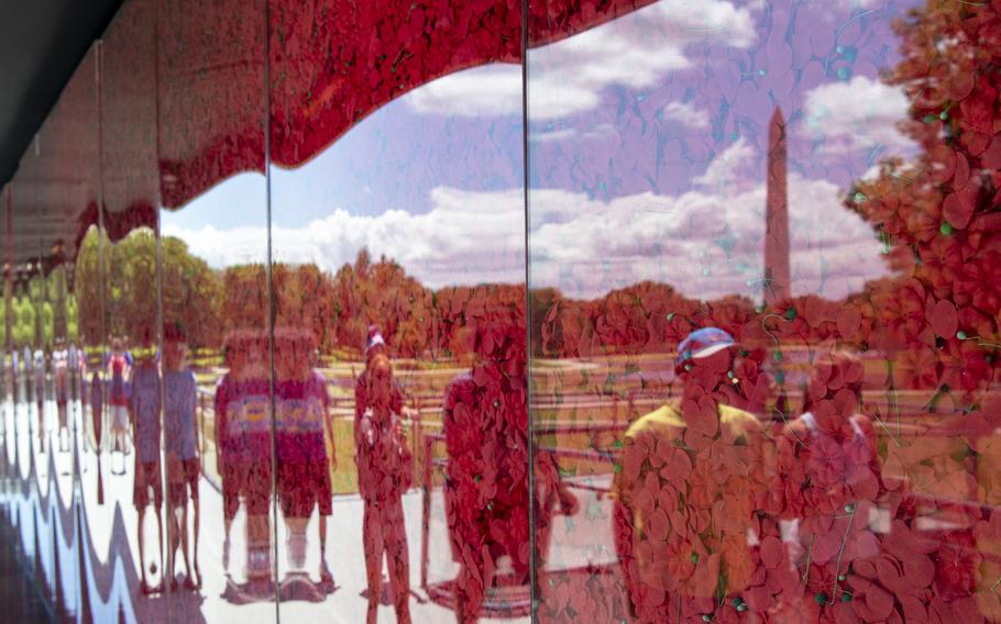 The reflection of visitors and the Washington Memorial in the background is seen on the glass panel encasing more than 645,000 fabric poppy flowers at the USAA Poppy Wall of Honor on Saturday, May 28, 2022, in Washington D.C.