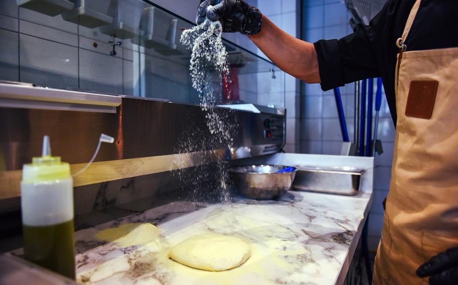Pizza dough is prepared by a cook.