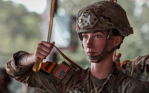 Close-up view of a soldier in camouflage uniform and helmet holding a strap over her shoulder while preparing for an aiborne operation.