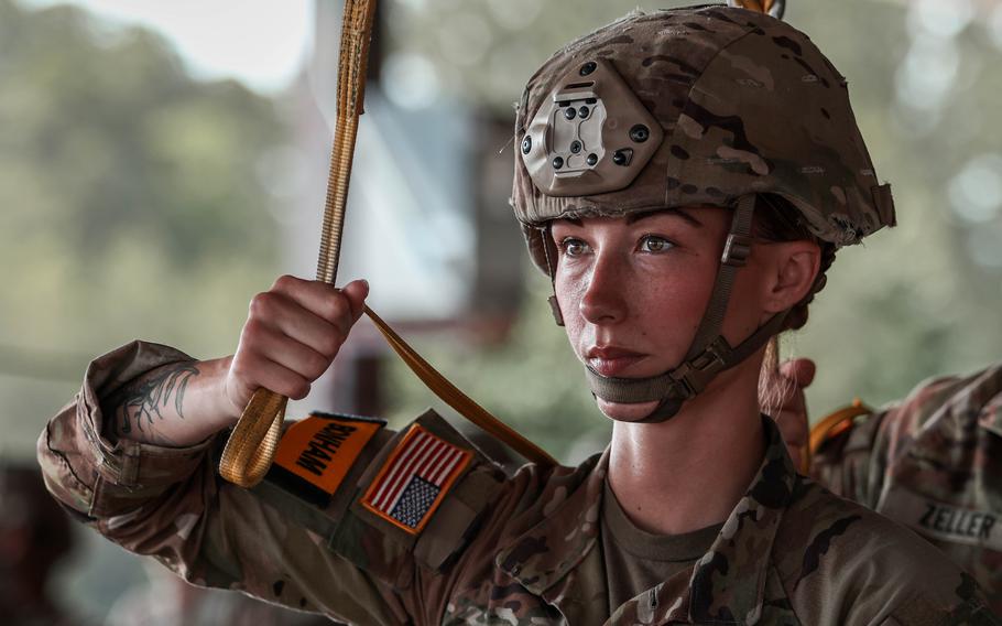 Close-up view of a soldier in camouflage uniform and helmet holding a strap over her shoulder while preparing for an aiborne operation.