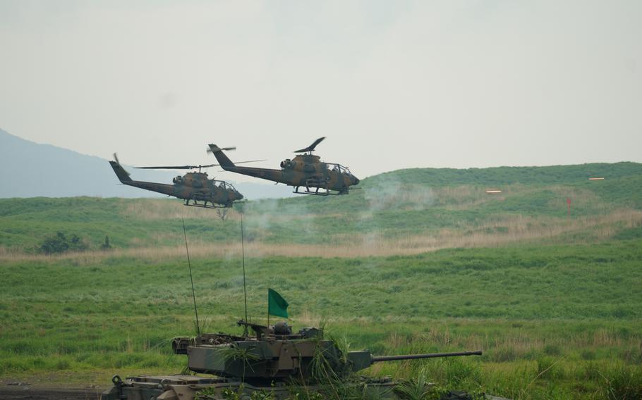 Japan Ground Self-Defense Force tanks perform live-fire drills in front of spectators while helicopters fly in the background.