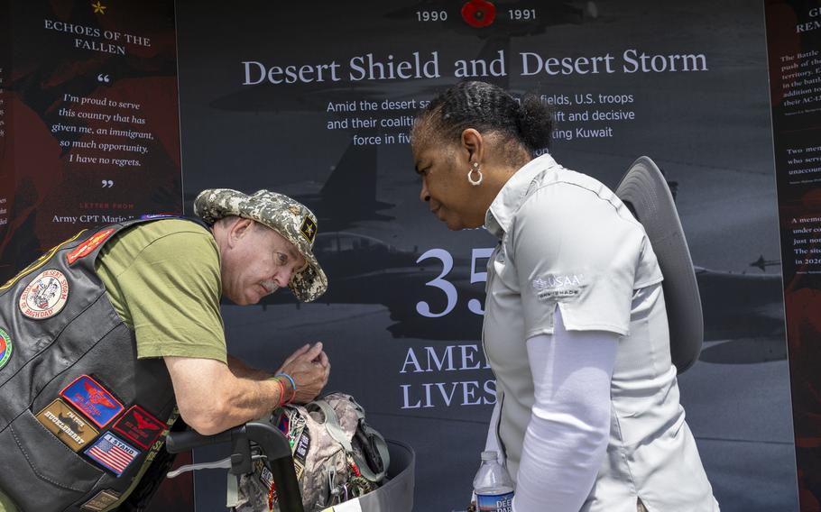 A man on the left pauses as a woman on the right looks on; both stand before a display about Operations Desert Storm and Desert Shield.