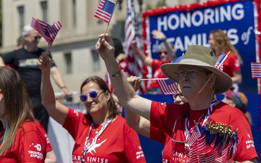 Marchers wearing red shirts for the Gary Sinise Foundation wave American flags.