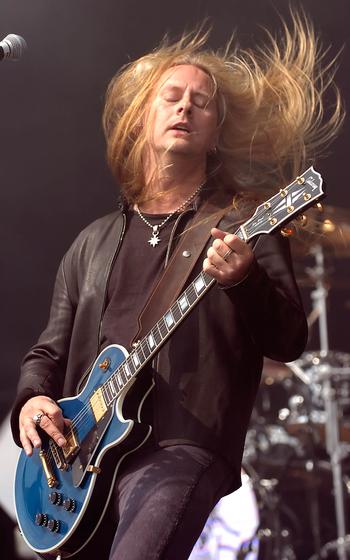 A man playing a guitar, with his long blond hair waving back and forth.