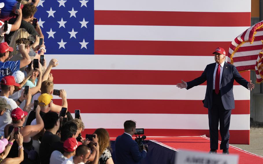President trump standing in front of a giant flag of the United States.