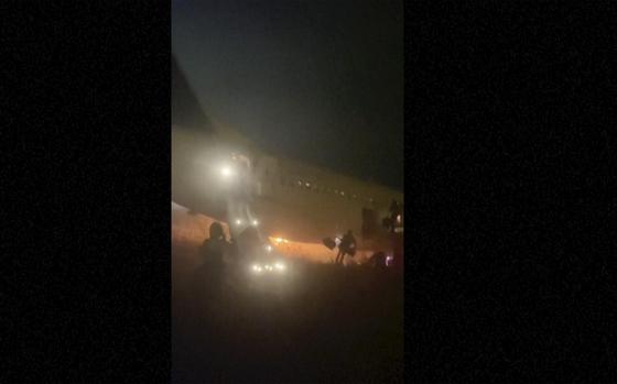 In this grab taken from video people jump down emergency slides, running from a plane, in Dakar, Senegal, Wednesday, May 8, 2024. A Boeing 737 plane carrying 85 people caught fire and skidded off a runway at the airport in Dakar, Senegal’s capital, injuring 10 people. (Cheick Siriman Sissoko via AP)