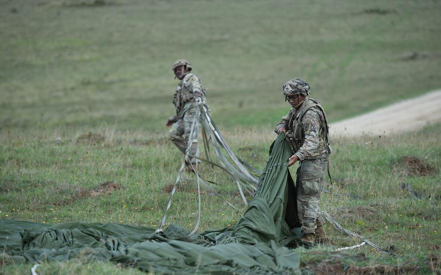 Soldiers with the 173rd Airborne Brigade gather parachutes that dropped an M119A3 howitzer and a tactical vehicle from a C-130 aircraft at the Hohenfels training area in Germany, Sept. 8, 2022. The heavy equipment was dropped using five separate parachutes and packaged with cardboard to soften the landing.  