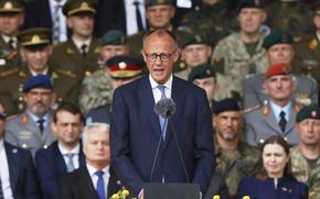 Friedrich Merz speaking in a blue suit in front of a podium with a microphone.