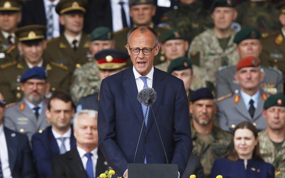 Friedrich Merz speaking in a blue suit in front of a podium with a microphone.