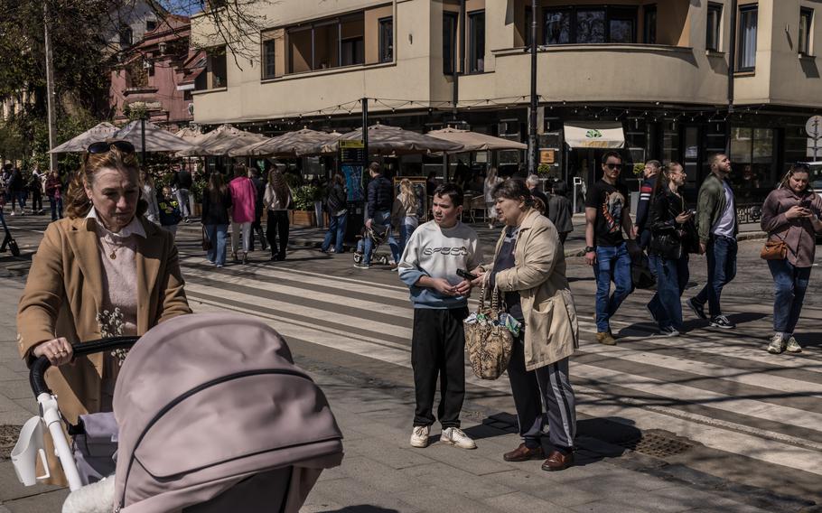 A boy and his grandmother walk in the city with other pedestrians.