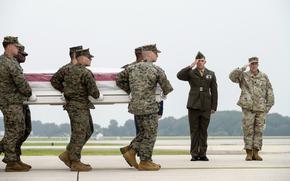A group of Marines carries a casket on a runway as two others salute.
