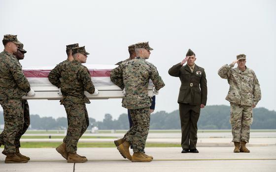A group of Marines carries a casket on a runway as two others salute.