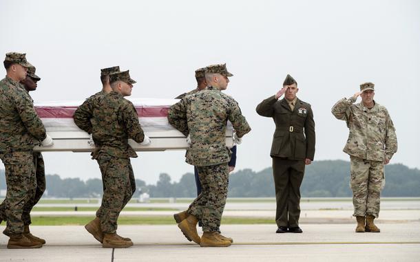 A group of Marines carries a casket on a runway as two others salute.