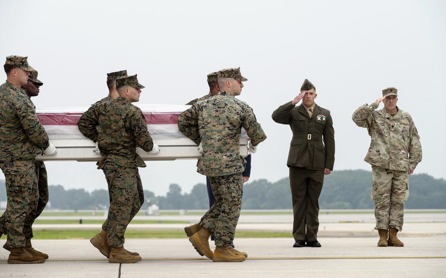A group of Marines carries a casket on a runway as two others salute.
