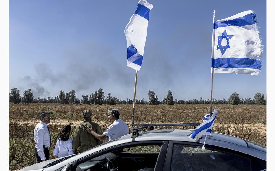 A family visit a soldier, as smoke rises over the Southern Gaza Strip seen from a position on the Israeli side of the border on May 24, 2024 in Southern Israel.