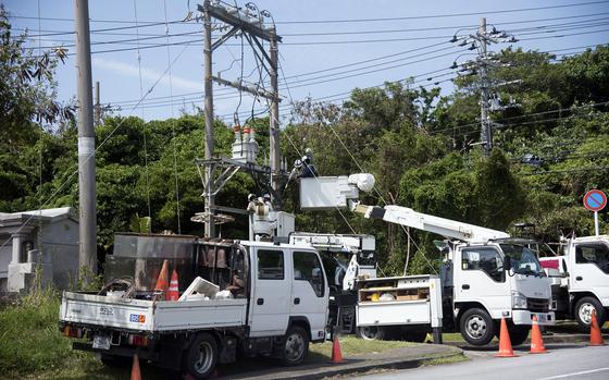 Multiple white trucks, including a couple with bucket lifts,  gather around utility poles outside Camp Courtney.